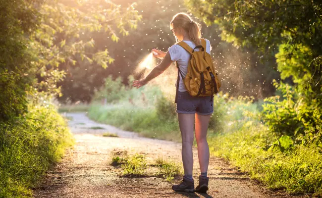 Hiker applies mosquito repellent spray to arm